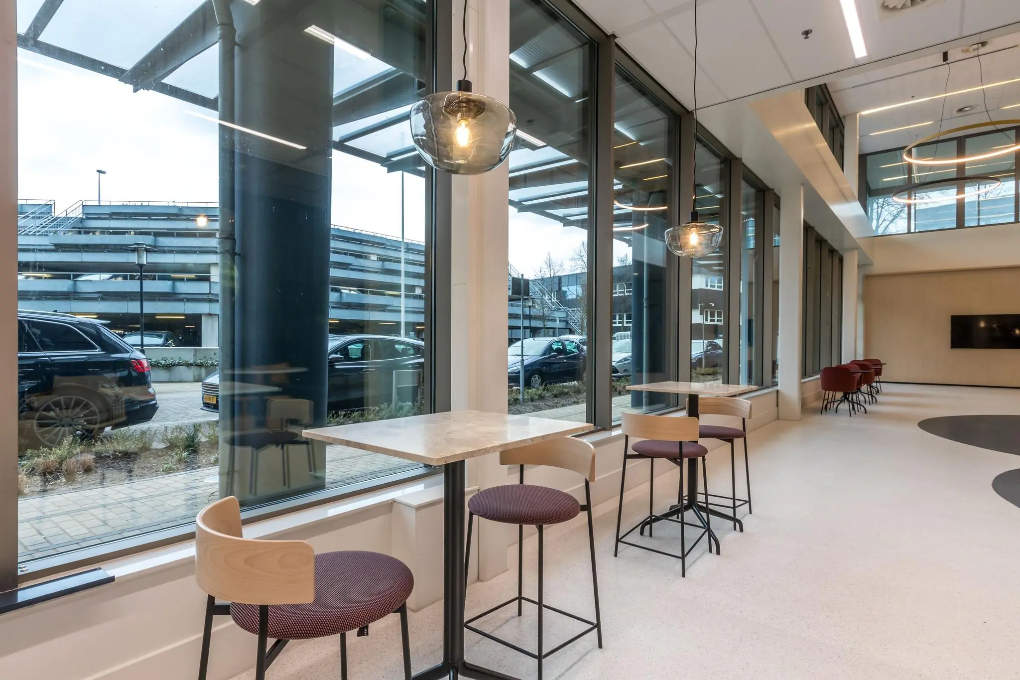 Moderne zithoek met hoge tafels en barkrukken bij grote ramen in een kantoorpand aan de Vliegend Hertlaan.